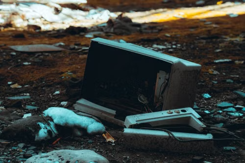 A CRT monitor and discarded electronics lying on a littered landfill